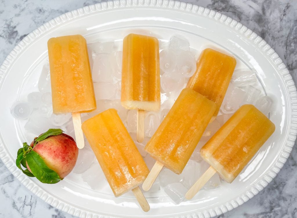 These adult only winesicles are made with 3 simple ingredients blended together-peaches (fresh, frozen, or canned), orange juice, and white wine. They are quick and simple to make and are my favorite way to cool off in the summer. Picture it- the hot sun, a pool, and a cold peach winesicle. Yes, please!